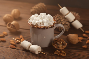 cup of hot cocoa with marshmallows, cone, nuts and cinnamon on wooden background