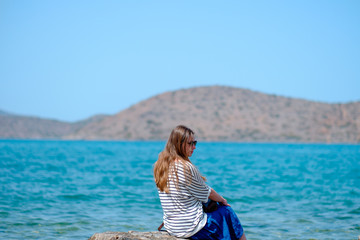 Fototapeta na wymiar young beautiful girl sitting on a pier looking at the sea and mountains