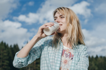 Portrait of Young woman drinks milk or yogurt with plastic bottle on nature background
