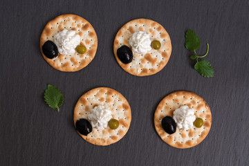 Snacks with a cracker of cheese and black olives on a plate of slate