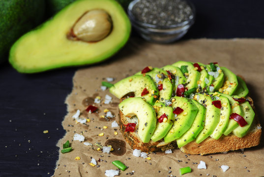 Avocado toast on rustic paper. It contains red chilies,salt,olive oil,peppers and chia seeds on dark background.Close up,copy space