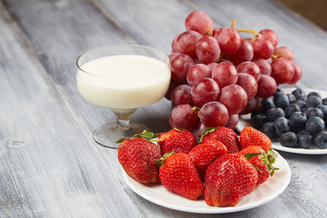 Strawberry, blueberry with yogurt and grapes on a gray wooden background