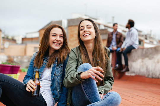 Two young female having fun and drinking beer sitting on the floor.