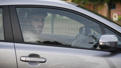 Serious young man or teenager driving car and looking at camera