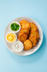 Potato pancakes, latkes or boxty and sauces from sour cream, yogurt, apple sauce and finely chopped green onion isolated on a blue background