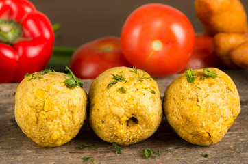 Bolon, an ecuadorian typical food with a blurred tomato and pepper behind, over a wooden table