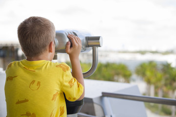 Fototapeta na wymiar Back view on kid boy with tourist binoculars looking into distance. Child exploring and telescope look. Binocular for tourist.