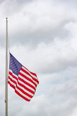 American flag flying at half mast or half staff against cloudy sky
