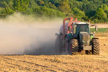 Grüner Traktor mit rotem Anhänger wirbelt eine Staubwolke auf dem Feld auf, closeup