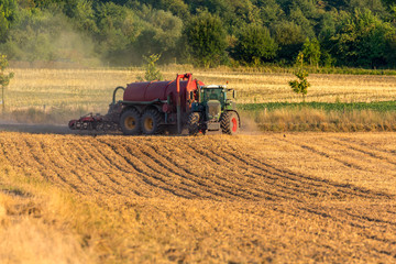 Fototapeta premium Grüner Traktor mit rotem Anhänger biegt in ein Feld ein, um es zu düngen
