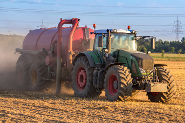 Grüner Traktor mit einem roten Anhänger voller Dünger kultiviert ein Feld, closeup