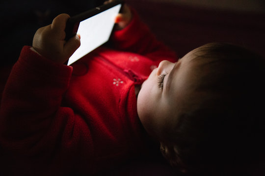 Baby using a mobile phone lying down on a bed