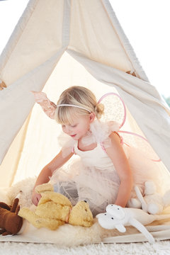 Adorable little girl playing dress up in a teepee tent in living room