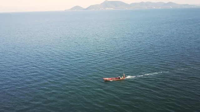 Aerial camera showing a small fishing boat motoring through the sea and orbits around it to show more islands in the distance as the camera tracks with the boat.