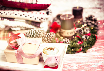 New Year and Christmas composition with a cup of cappuccino, wrapped gift, pine branches, coffee candles, warm clothes. red colour wooden background