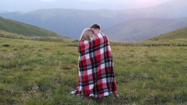 The couple wrapped in plaid stand in the meadow and enjoys each other
