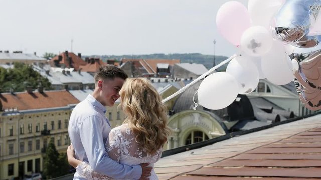 Couple holding some ballons on the rooftoop hugging and looking at city