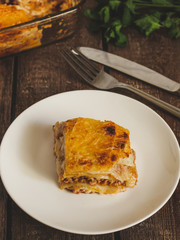 Lasagna on a white plate on a wooden table surrounded by products