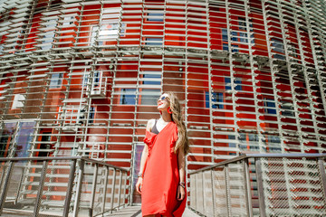 Lifestyle portrait of a woman in red dress in front of the modern building facade outdoors