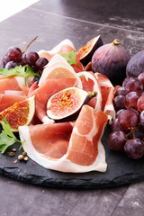 prosciutto with parsley, figs and grapes on a black stone food tray.