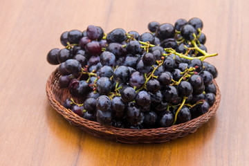 Ripe grapes in wicker basket on wooden table