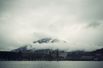 Naklejka na ściany i meble Paisaje invernal suizo con las montañas de Los Alpes cubiertas de niebla densa blanca con edificios en primer término.