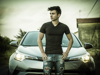 Portrait of young man or teenager leaning on his new stylish polished car, outdoor