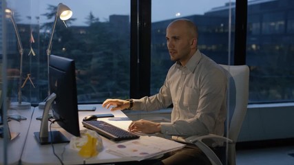 Business entrepreneur working late at night, looking over graphs and working at his computer. - Powered by Adobe