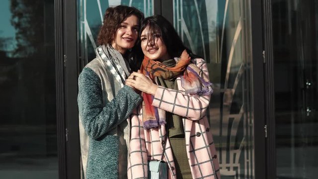 girlfriends hugging and smiling on the background of modern architecture. girl in autumn coat posing on camera. Friends spend time together