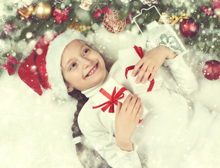 Obraz na płótnie Canvas girl child lie in christmas decoration on white fur, yellow toned, face closeup, dressed in santa hat, winter holiday concept, xmas tree