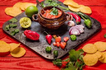 Homemade salsa with ingredients on black stone desk on red rustic background, tomato, pepper, onion, chili, habanero, coriander leaf. Mexican food concept