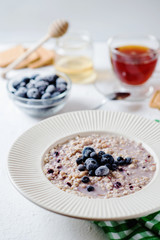 delicious, hearty and healthy breakfast, oatmeal on milk with berries - blackberries, blueberries, honey and black tea on a light background