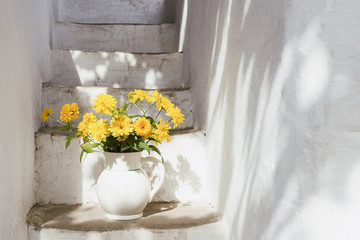 Fresh yellow flowers in white vase on white stairs