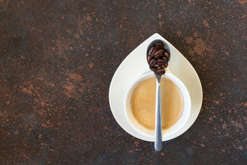 White espresso cup of coffee with a spoon of coffee beans on a dark brown background in Scandinavian style minimalism with a copy of the space top view flat