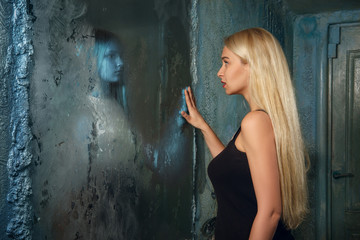 Frightened young woman looking to the mirror and seeing in reflection a ghost girl