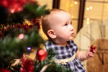 A cute little girl in front of the fir-tree and fireplace with candles and gifts. New year's eve. Christmas eve. Cozy holiday at the fir-tree with lights and gold decor.