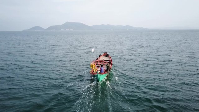 Aerial camera at low altitude following a small wooden fishing boat as it motors over the blue sea towards Kep, Cambodia from Koh Tonsay (Tonsai), or Rabbit Island.