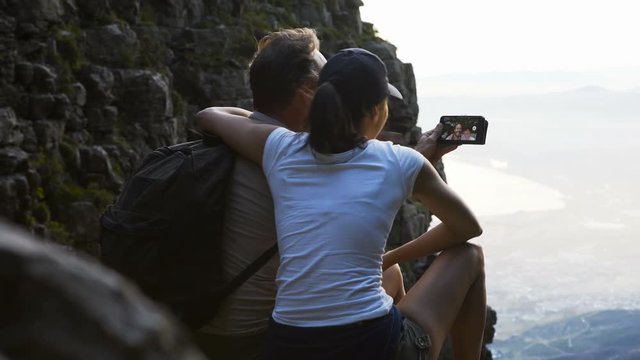  Happy active couple looking at view from rocky hill top & making video call