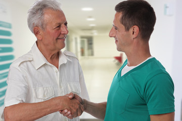 Obraz premium Smiling male doctor giving handshake to senior male patient. Health care concept