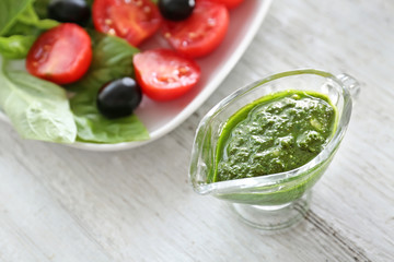 Gravy boat with basil pesto sauce on wooden table
