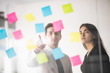 Two businesspeople discussing and planning concept. Front of glass wall marker and stickers. Startup office.