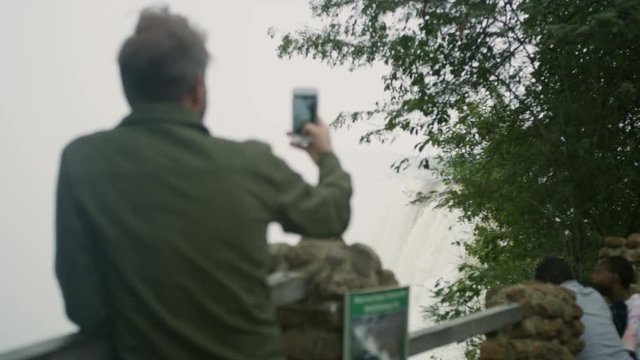 Portrait smiling man on African vacation filming Victoria Falls on smartphone