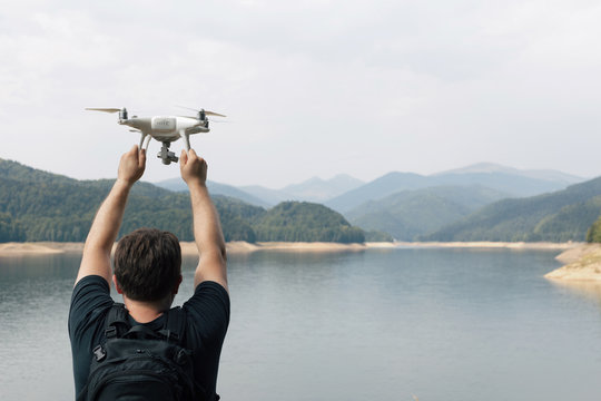Man is holding white drone near Lake Vidraru at Fagaras Mountains. Romania