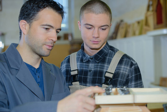 skillful carpenter working with male apprentice in workshop