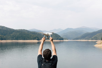 Man is holding white drone near Lake Vidraru at Fagaras Mountains. Romania