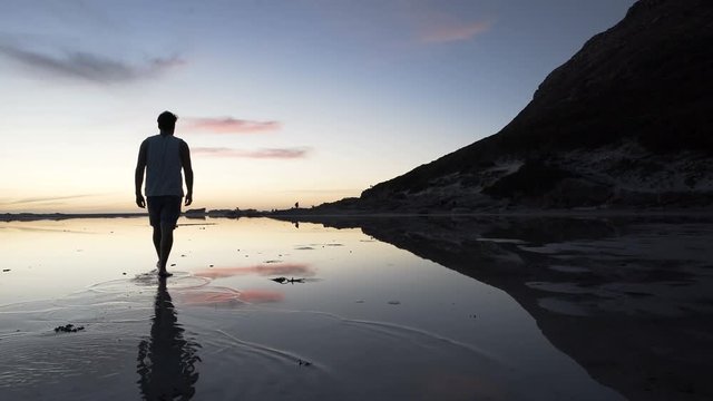 Man walking on beautiful sandy beach at sunset stops to take a photo of view