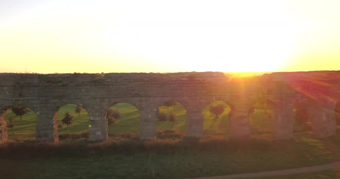 Video from above. Aerial view of the ancient Roman Aqueduct at sunset. Old ruins surrounded by a green public Park. Rome, Italy.
