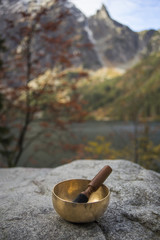 A Himalayan singing bowl on a boulder with mountains and a lake in the background. 