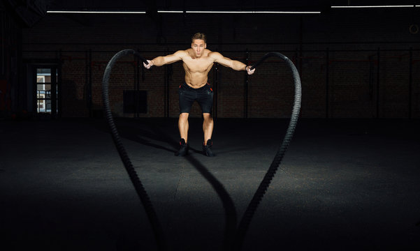 Fitness man workout with battle ropes at gym. training exercise fitted body in club. Torso.