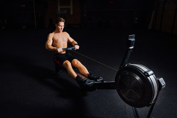 Fitness young man using rowing machine in the gym - obrazy, fototapety, plakaty